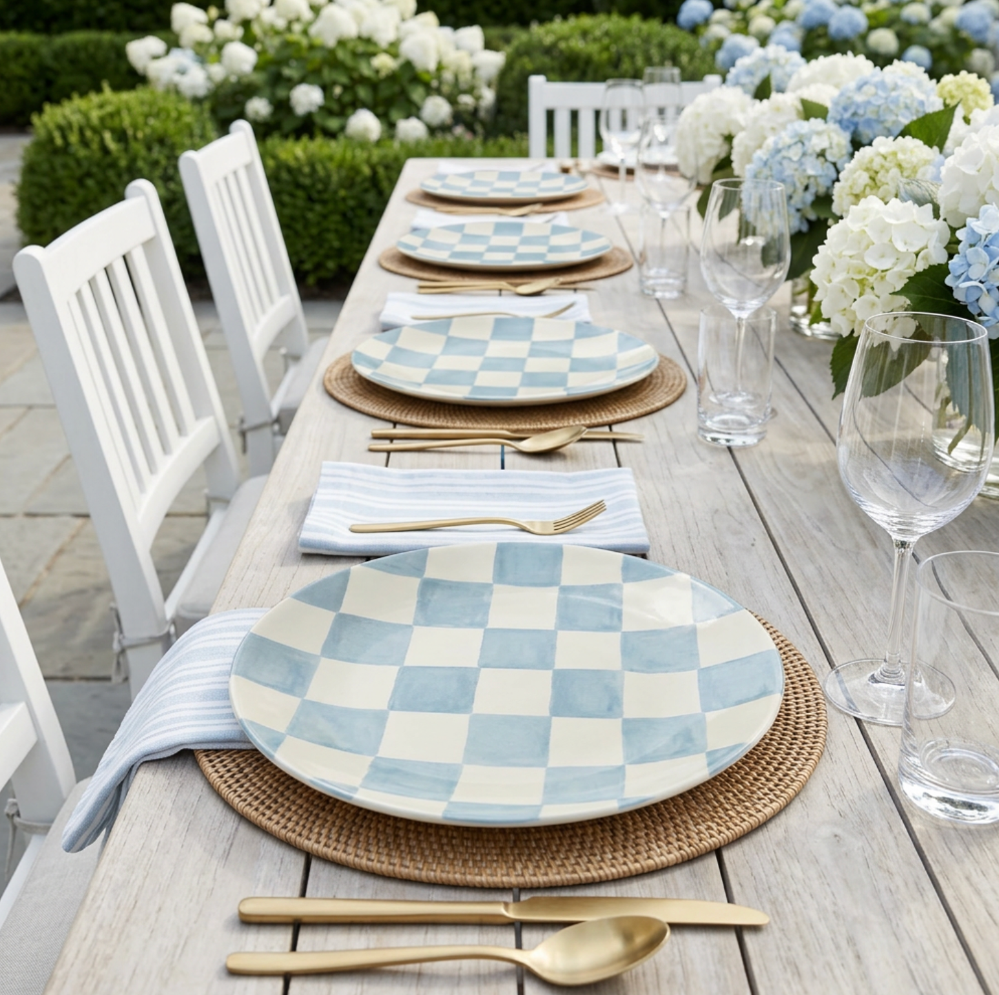 Light blue checkered melamine dinner plates on an outdoor table with gold flatware and hydrangea centerpieces.