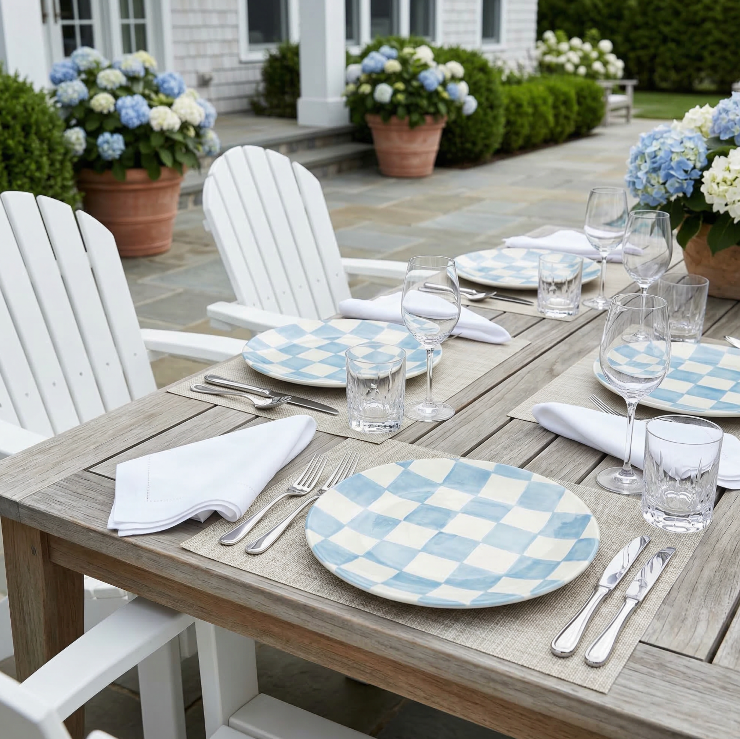 Light blue checkered melamine dinner plates on an outdoor wooden table with glassware and napkins.